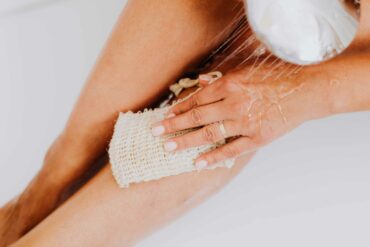 Eine Frau duscht ihre Beine ab und wäscht sich mit einem Duschschwamm aus Stoff.