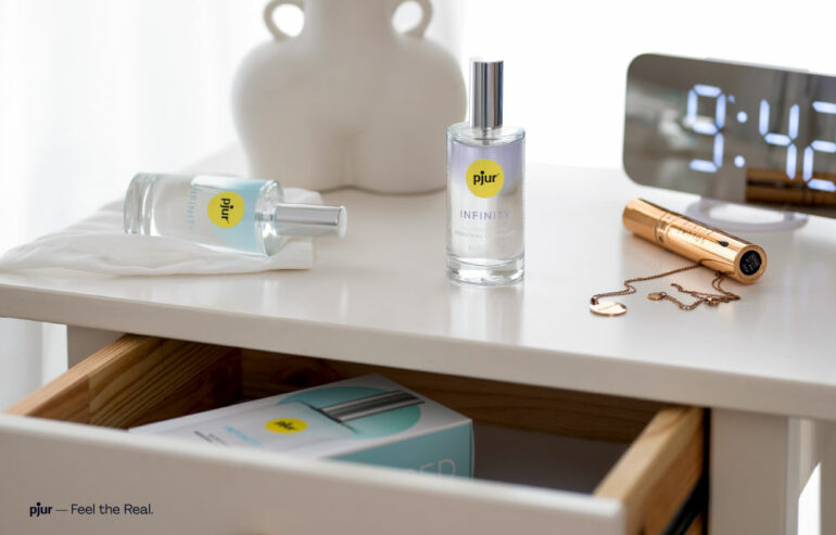 Ein Gleitgel in einer Glasflasche steht auf einem minimalistisch und modern dekoriertem, weißen Nachtschrank.