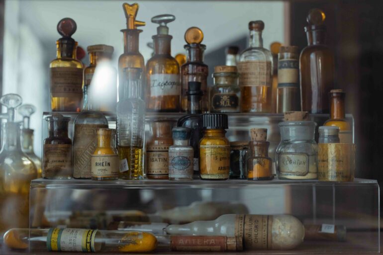 In front of a mirror, there are various old bottles, tubes, and flacons. Everything appears as if from an old pharmacy.