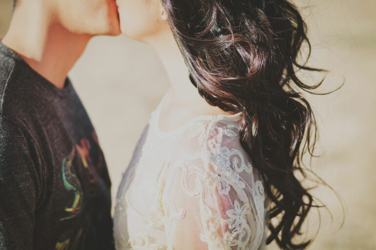 Ein Pärchen, bestehend aus einem Mann und einer Frau, steht sich gegenüber und küsst sich.