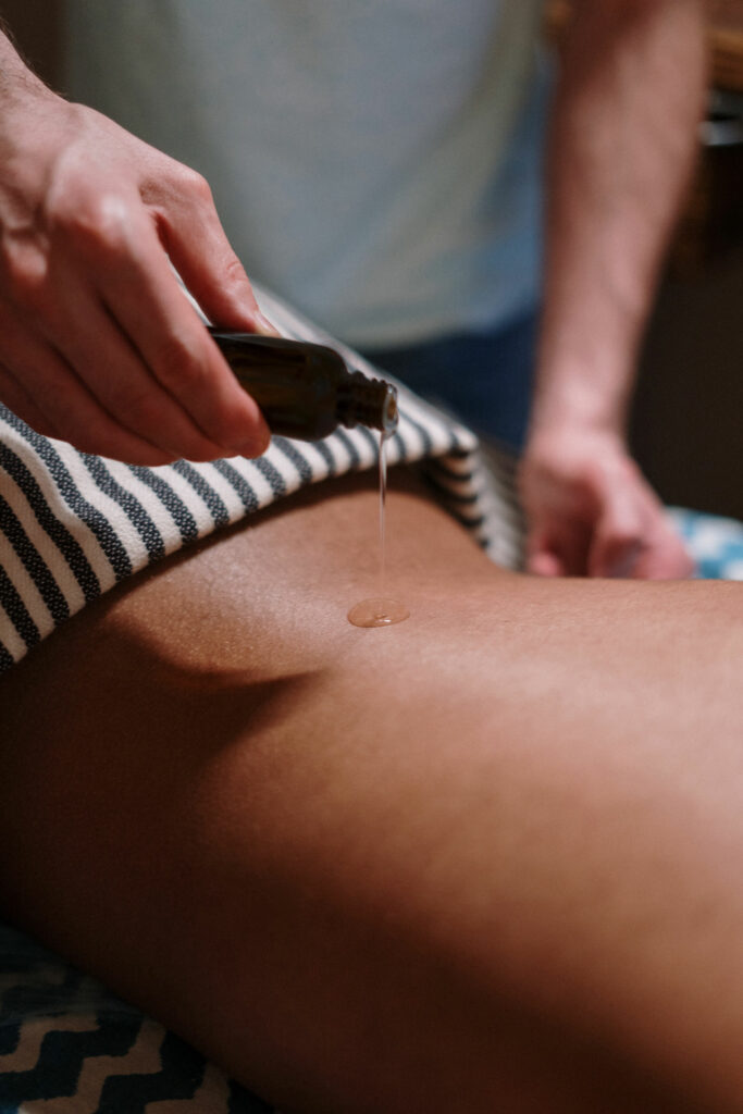 A person is dripping some personal lubricant from a bottle onto the back of another person for a massage.