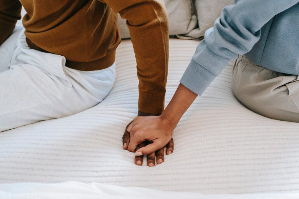 Two people holding hands on the bed.