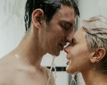 Ein Bild, das eine intime Umarmung und, einen liebevollen Kuss zwischen Mann und Frau in der Dusche mit freiem Oberkörper zeigt.
