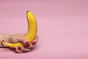 Pinker Hintergrund und in vom Vordergrund ist eine Hand, die eine Banane hält.