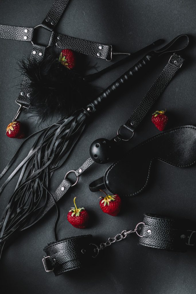 schwarze BDSM Spielzeuge, rote Erdbeeren verteilt, Schwarzer Hintergrund