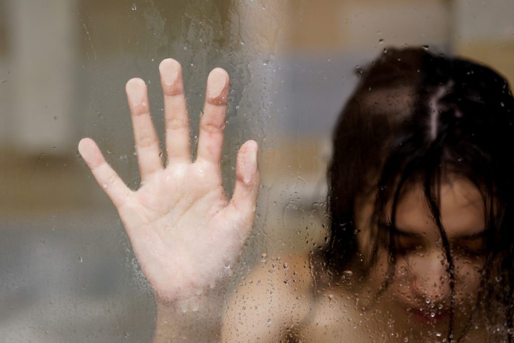 Woman under a shower leaning her hand against the glass